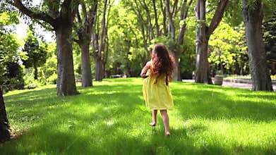 Happy little girl with yellow dress running barefoot on green grass in the park
