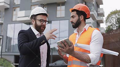 Construction manager and architect man are discussing the construction plan of the modern business center. They checks