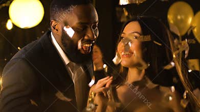Smiling multiracial friends dancing at night club party under falling confetti