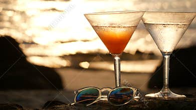 4K. Cocktail glass with water droplets on the beach with golden wave reflection with heart bokeh during the sunset time