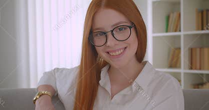 Closeup portrait of young redhead female in glasses turning and looking at camera smiling with excitement sitting on the