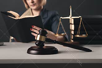 Woman lawyer reading professional books in office. Wooden gavel and libra on the desk.