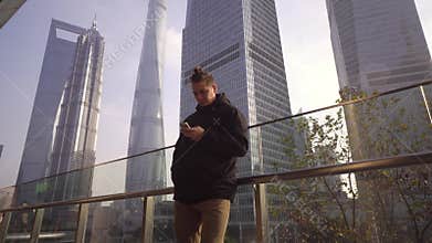 A young man in a black jacket uses a telephone on the background of skyscrapers in Shanghai, China