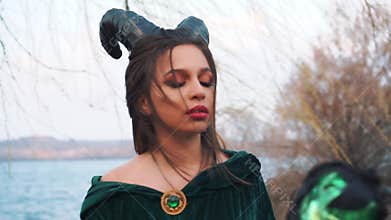 Evil magic queen creates magic spell against enemy, black witch in long green emerald dress mantle beats magic stick on