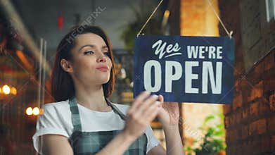 Female manager opening coffee shop in morning hanging open doorplate smiling