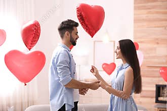 Happy young couple in room decorated with heart shaped balloons. Valentine`s day celebration