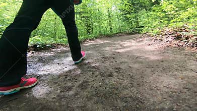Low angle footage of feet walking on forest trail.