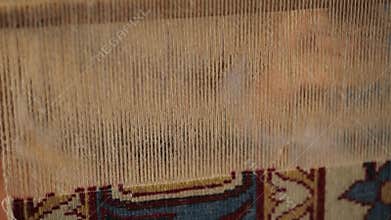 A woman sews an oriental carpet. Close-up of hands work behind a loom