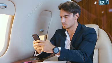 Young handsome chief banker director businessman using smartphone durung flying in airplane. Successful business man