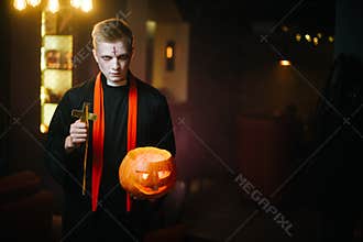 Guy as a priest holds a cross and a Halloween pumpkin