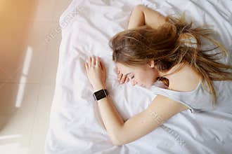 Portrait of young woman sleeping with smart watches on hand in white bed