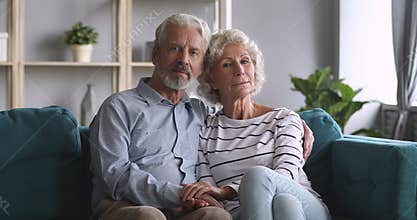 Serious happy senior couple bonding looking at camera on sofa