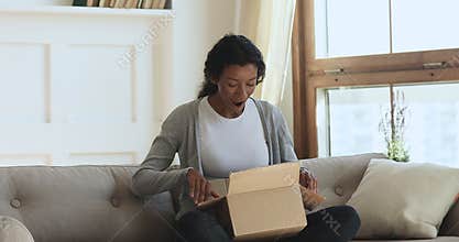 Amazed happy young african woman open parcel at home