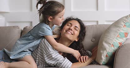 Cute funny kid daughter tickling kissing mum playing on sofa