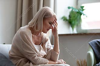 Sad mature woman sitting alone at home feeling headache depression