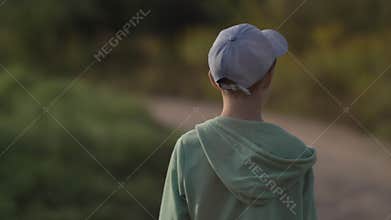 Back view of a boy in a cap is walking along a country road outdoors