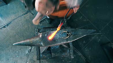 One blacksmith shapes knife on anvil, using hammer.