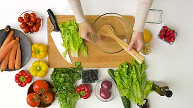 Woman adding lettuce to salad bowl at home kitchen
