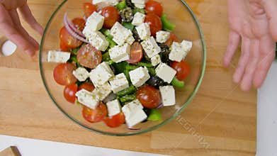 Hands turning bowl of vegetable salad with feta