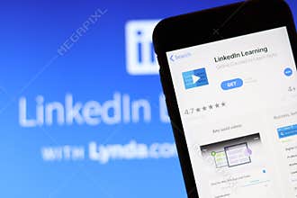 Mobile phone with LinkedIn Learning icon on screen close up with LinkedIn website on laptop. Blurred background.