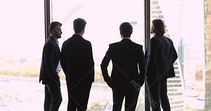 Back view at successful businessmen looking through big office window