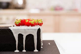 Birthday cake black colored with white glaze and decorated by strawberry. Chocolate cake with fruit