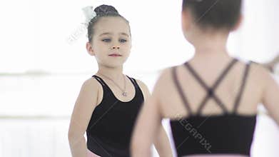 Little ballet girl in leotard are posing in front of the mirror