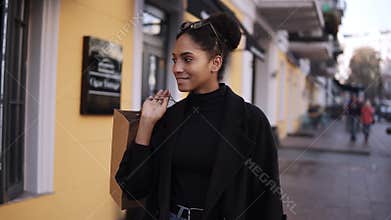 Portrait of an attractive mixed race girl smiling while walking down the street with little brown bag. Happy young woman