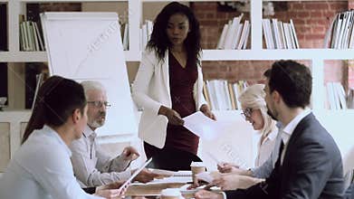 Black female boss give papers to employees group at meeting