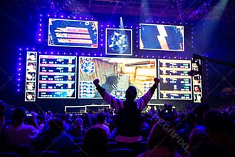 Big esports event. Video games fan on a tribune at tournament`s arena with hands raised. Cheering for his favorite team.