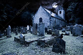 Old graveyard with ancient tombstones grave stone and old church front of full moon black raven dark night spooky horror