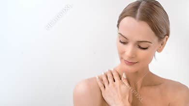 Beautiful bare woman smiling gently stroking soft young skin having positive emotion medium close-up