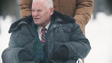 An old man veteran sitting in a wheelchair being driven by his son