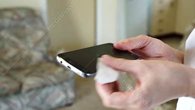 Person cleans and wipes smartphone inside domestic home, fixed close up