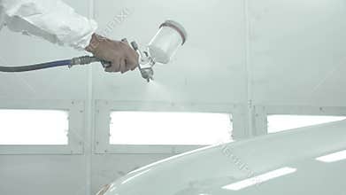 Process of painting a white car in a spray booth. Man using a spray gun