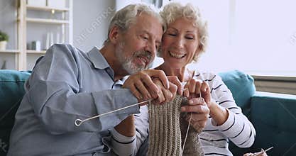 Happy grandparents couple having fun knitting scarf together at home
