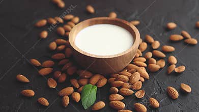 Almond seeds with bowl of fresh natural milk placed on black stone background