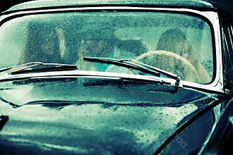 Young people driving retro car in the rain