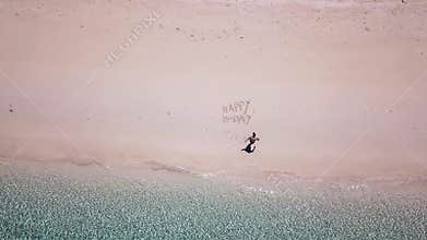 A drone shot of a man lying on a pink sand beach next to `Happy Birthday` sign on a small island near Maumere, Indonesia. Happy