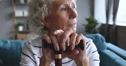 Focus on older hoary woman holding hands on walking stick.