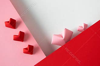 Pink and red origami hearts on white background and paper borders, top view. Creative postcard for Valentine`s day or wedding
