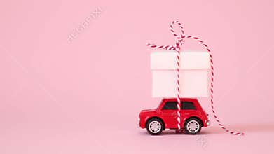 Red retro toy car delivery gift box with ribbon bow on a pink background. Birthday, Valentine`s Day, Women`s Day concept