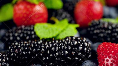 4k dolly video of camera moving over big assortment of berries and mint leaves. Big heap of strawberry, blueberry and