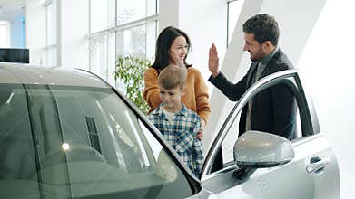 Young family with child buying car in dealership, man and woman doing high-five