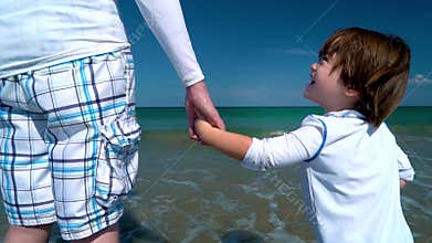 Toddler holding hands with his father at the sea shore