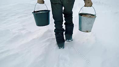 An elderly man with buckets in winter carries water from a well. Handheld shooting.