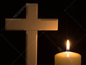 Burning candle under Jesus cross in a cemetery against black background.