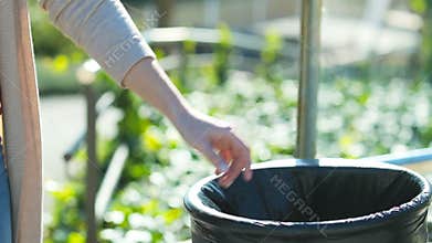 Woman hand throwing trash into bin in a park in sl