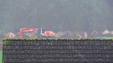 Digger machine moving earth with two workers walking around, construction site during rainy weather in rucphen, The Netherlands, 4