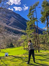 Vertical shot of a female playing golf in the green field with mountains in the background